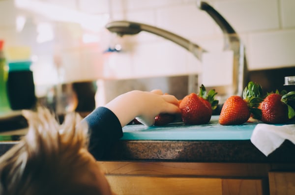 small child trying to reach strawberries on a kitchen bench